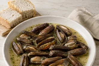 قواقع طويلة داكنة مفتوحة في طبق أبيض مملوء بصلصة بوزارا فاتحة مع بقدونس، وبجواره خبز وملعقة