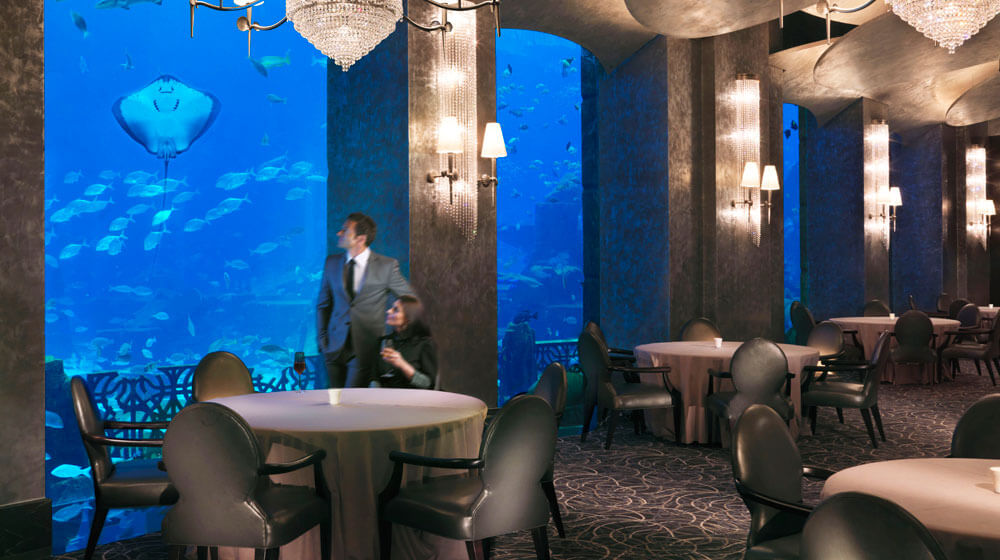 طاولات قاعة Ossiano تواجه حوض Ambassador Lagoon المضاء في Atlantis