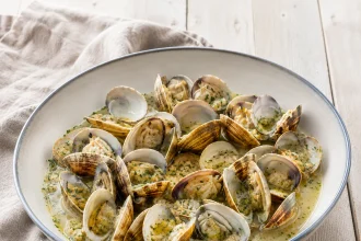 Geöffnete Venusmuscheln in heller Buzara-Soße mit Petersilie und Brot auf Holztisch
