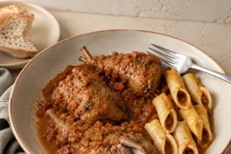 Quadratische Aufnahme von geschmortem Kaninchen in roter Gemüsesauce mit mehreren kurzen röhrenförmigen Pastastücken