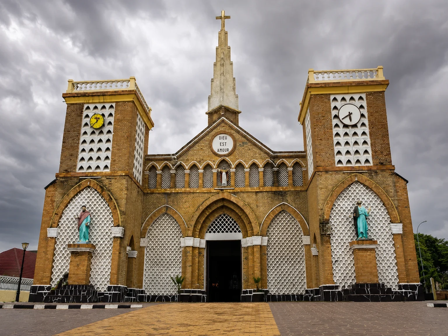 Kirchenfassade mit zwei Uhrtürmen und zentralem Kreuz unter dunklen Wolken in der Republik Kongo