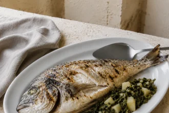 Ganze gegrillte Dorade mit knuspriger Haut neben Mangoldkartoffeln auf einer großen weißen Servierplatte