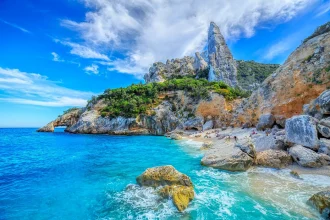 Heller Sandstrand mit klarem türkisfarbenem Wasser und natürlicher Küstenlandschaft