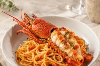 Quadratische Aufnahme von Spaghetti in roter Tomatensauce mit großen Stücken Langustenfleisch und Kräutern.