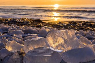 Transparente Blöcke von Jewelry Ice im warmen Sonnenaufgangslicht an einem dunklen Strand in Hokkaido