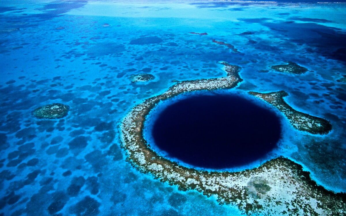 Luftaufnahme des Great Blue Hole als dunkler Kreis im türkisfarbenen Riff von Belize