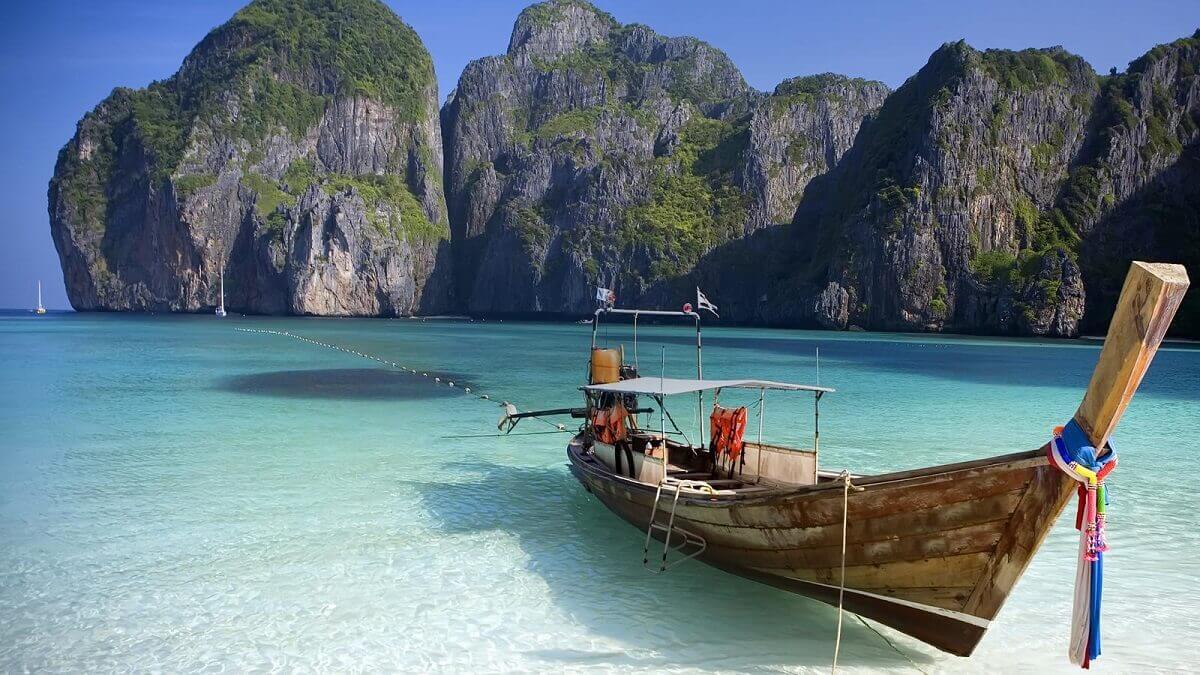 Bateau traditionnel dans les eaux turquoise de Maya Bay sous les falaises calcaires