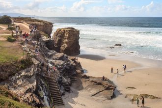 Visiteurs descendant l’escalier de la falaise vers la Praia das Catedrais à marée basse sur la côte galicienne