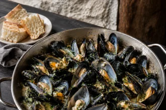 Padella quadrata piena di cozze aperte in fondo chiaro con aglio