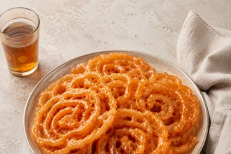 Zlabia algerine arancioni e lucide disposte a spirale su un piatto con tè