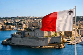 港の石造要塞を背景に風を受けるマルタ国旗