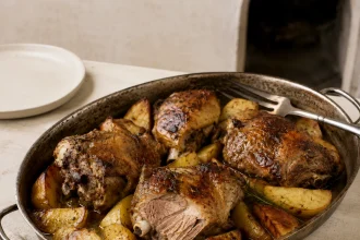 Goudbruin lamsgebraad met aardappelparten en rozemarijn in een donkere metalen braadslede