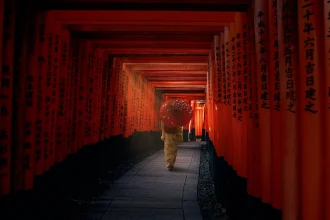 Osoba u kimonu sa crvenim suncobranom ispod vermilion torii kapija u Kjotu