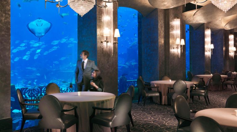 Stolovi u restoranu Ossiano okrenuti ka osvetljenom akvarijumu Ambassador Lagoon u Atlantis