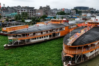 孟加拉国一处城市河港内停泊的橙色客船与岸边建筑