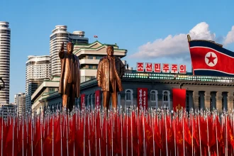 平壤铜像前排列红旗，朝鲜国旗悬于建筑上方